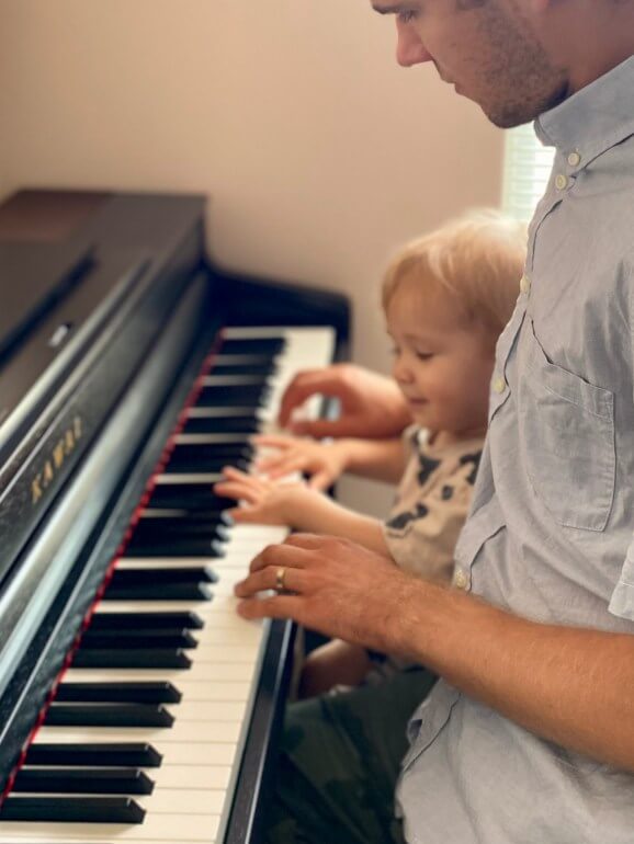 A very young beginner student attentively receiving piano instruction from his teacher at his home.